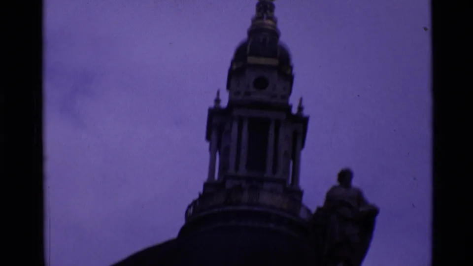 Soft 8mm frame of a London domed tower and nearby statue seen as dark silhouettes against the sky.