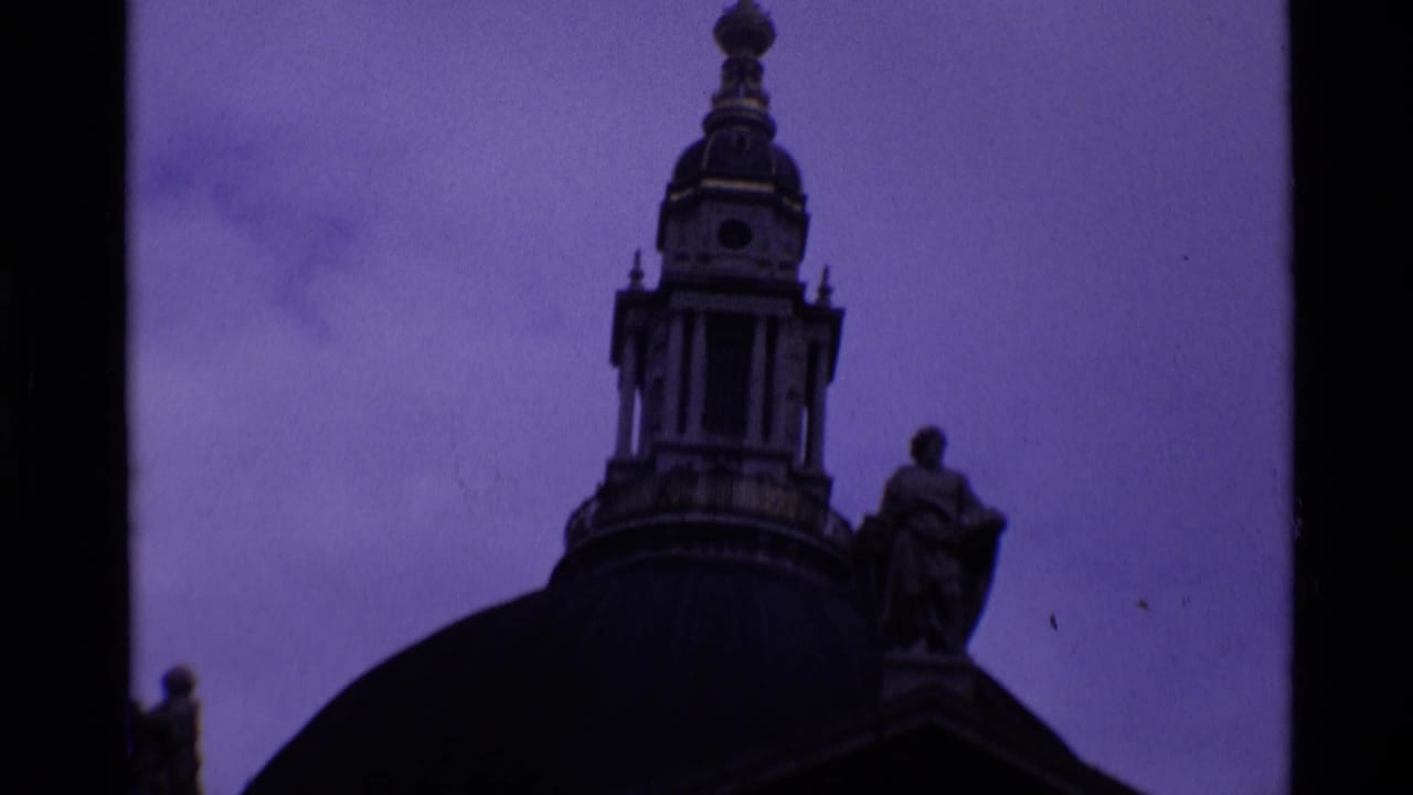 1969 8mm London footage showing the upper dome, lantern, cross, and statue details of St Paul's Cathedral at twilight.