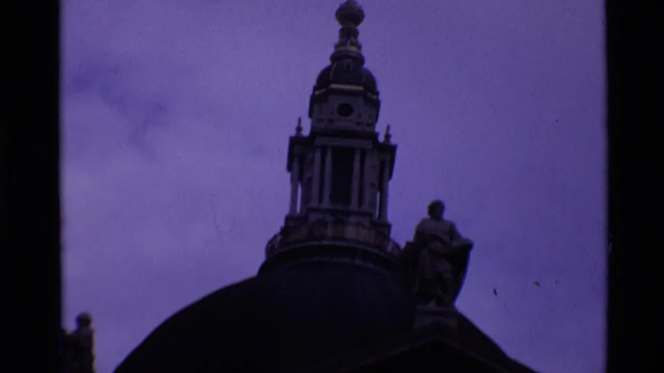 1969 8mm London footage showing the upper dome, lantern, cross, and statue details of St Paul's Cathedral at twilight.