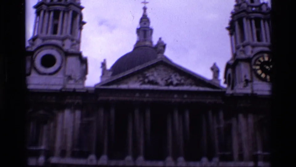 1969 London 8mm frame showing a classical church-like facade with towers, columns, dome, and clock face in soft purple-tinted color.