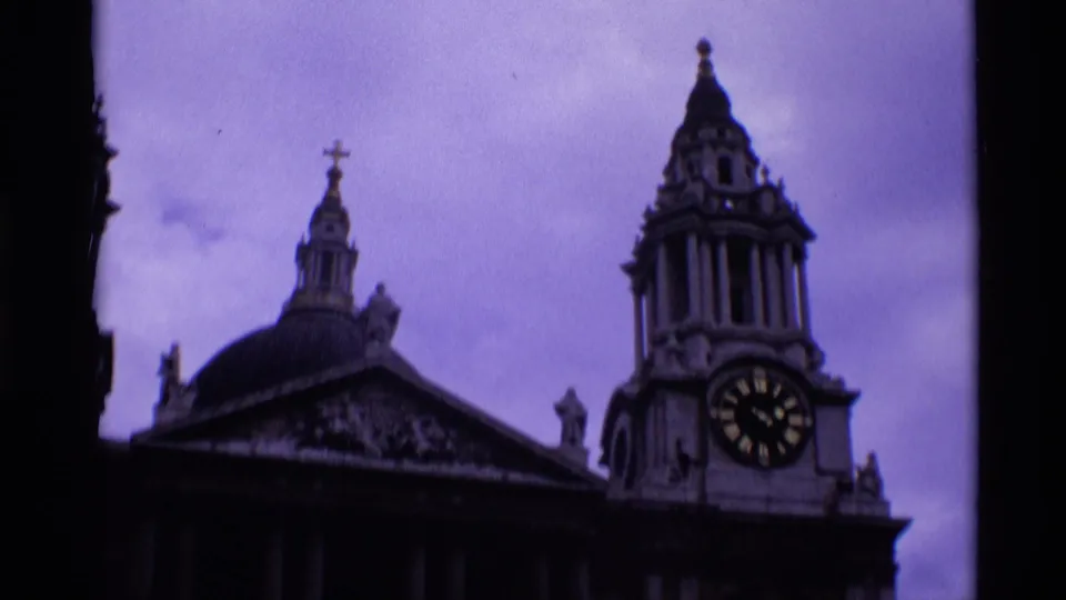 1969 London home-movie frame showing the right portion of a classical church-like facade with a clock tower and domed roofline.