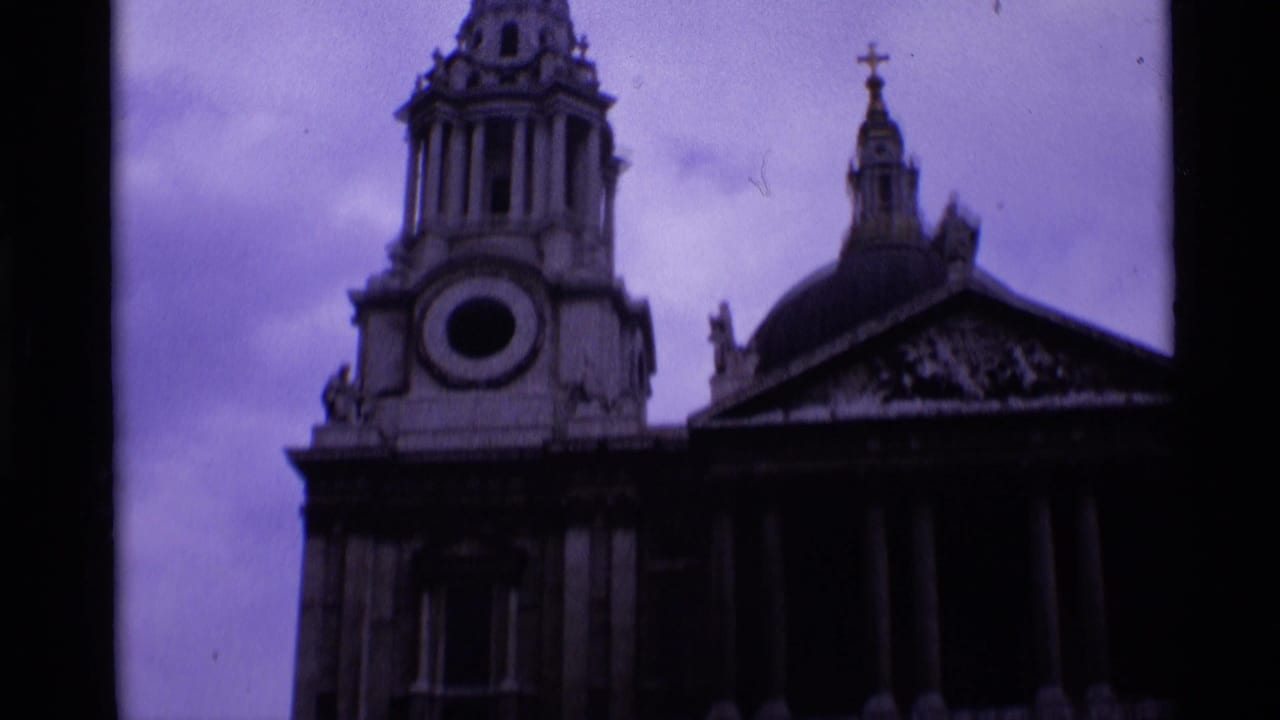 1969 London 8mm frame showing a low-angle view of a church steeple, cross, dome, and columned facade under a cloudy sky.