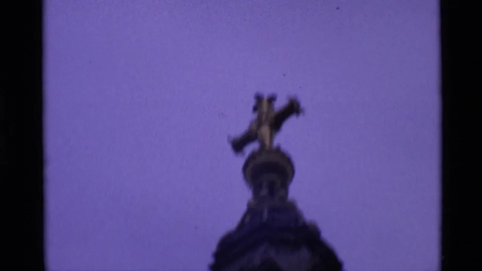 1969 London 8mm frame centered on a gilded sculptural figure atop a column, filmed from below against a pale sky.