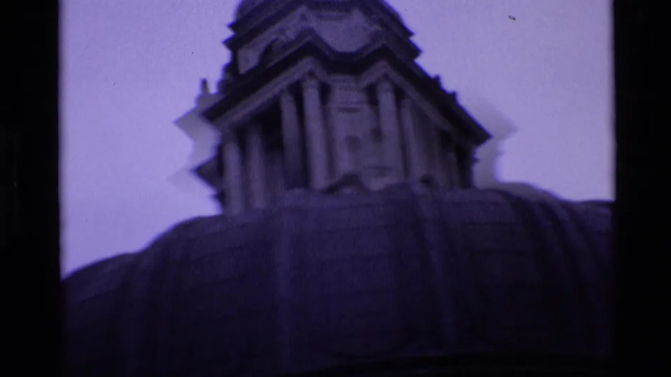 1969 London church exterior seen from below, with a dome, upper facade, columns, and dark roofline rendered in purple-tinted 8mm footage.