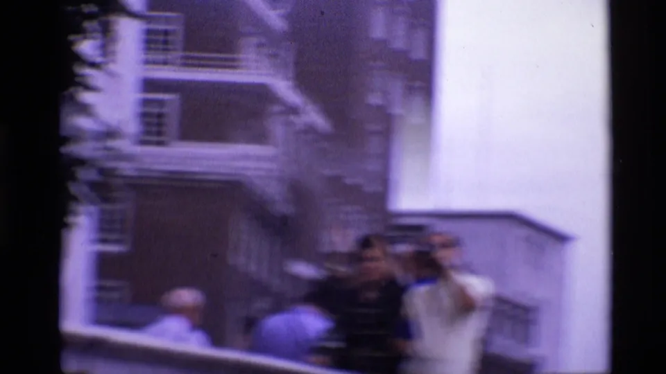 1969 London tourist scene with people near a railing, one appearing to hold a camera, with a historic facade behind them.