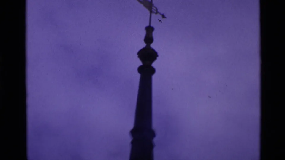 Tall pointed steeple in silhouette against a purple-blue sky, framed by the faded color and softness of 8mm film.