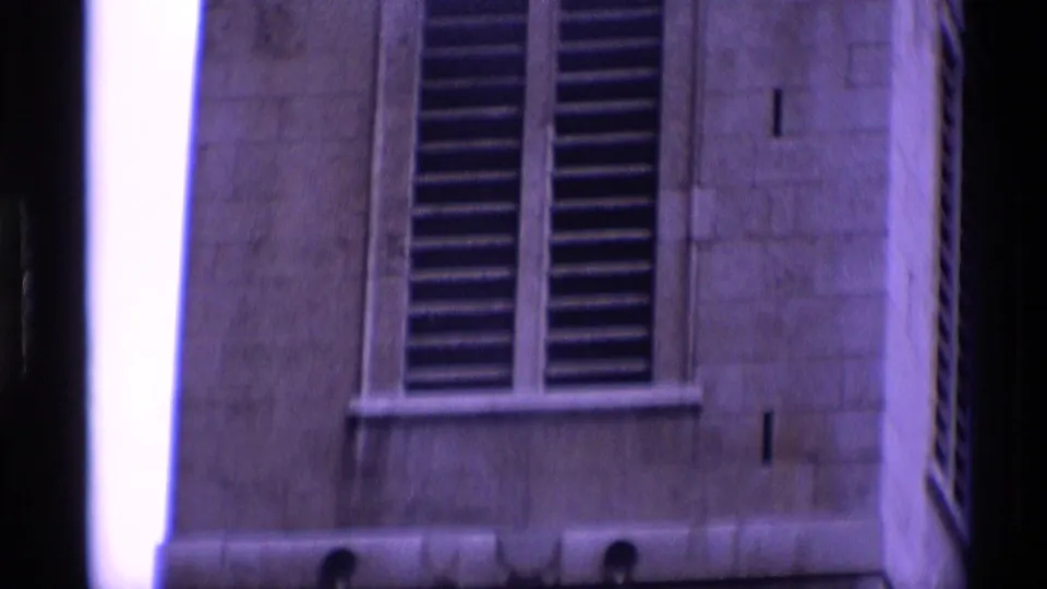 1969 London 8mm frame of a stone tower wall with a tall louvered window or shuttered opening.