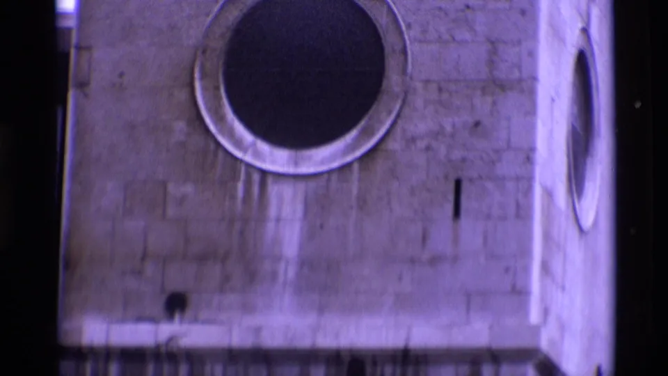 1969 London 8mm frame showing a round opening in a stone tower wall, with purple tint and gate-edge darkness.