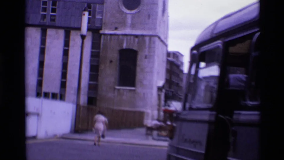 1969 London street view with stone buildings, a pedestrian walking away, and a classic bus at the right edge.
