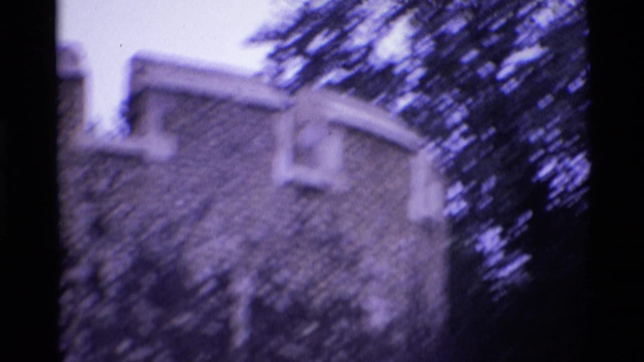Handheld 1969 London frame with castle-like stone wall, crenellations and surrounding tree cover.