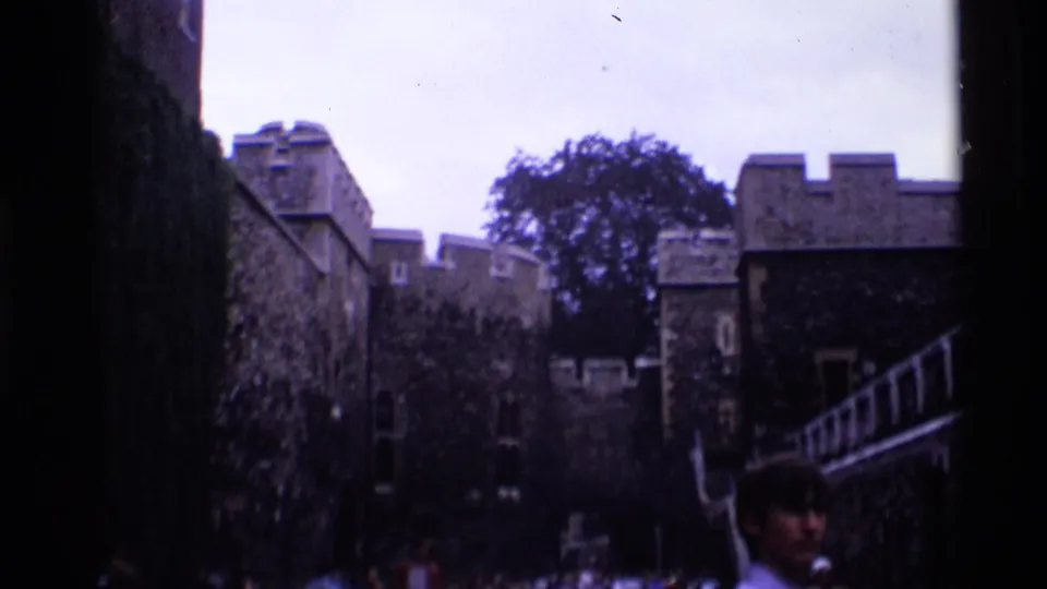 1969 London 8mm view of a historic courtyard with stone walls, battlements, trees and visitors present.