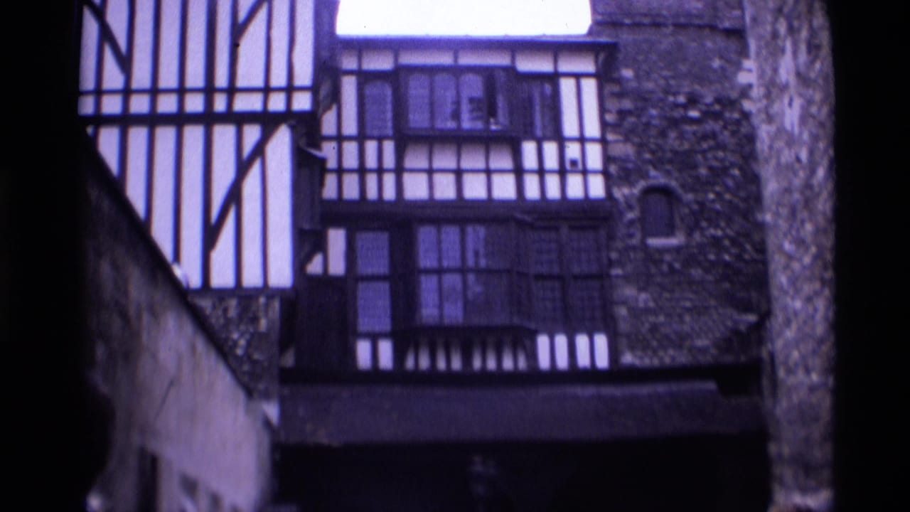 1969 London home-movie frame showing a half-timbered facade beside stonework and dark window bays.