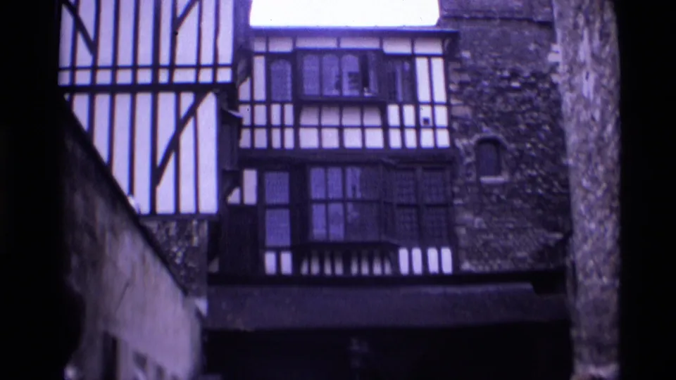 1969 London home-movie frame showing a half-timbered facade beside stonework and dark window bays.