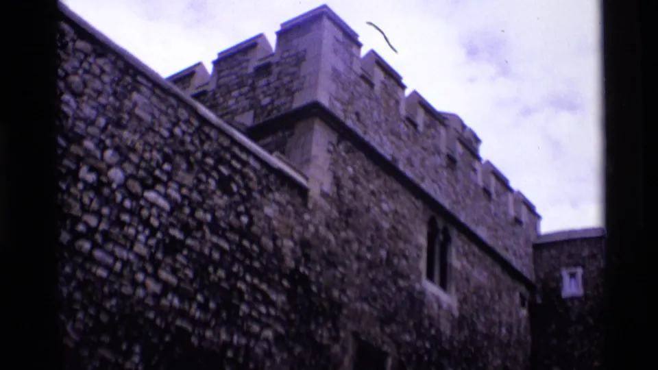 1969 London home-movie view of crenellated stone battlements and rough masonry beneath a cloudy sky.