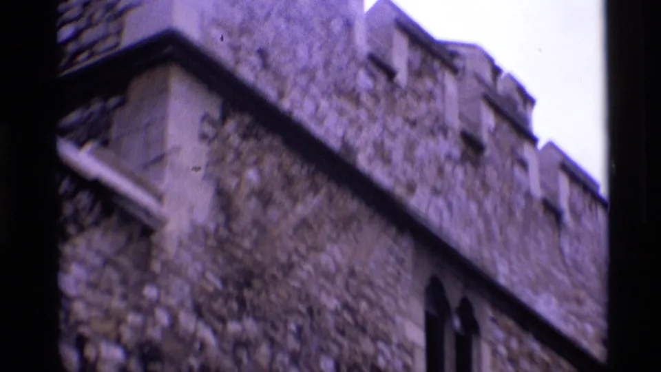 1969 London frame showing a closer handheld look at crenellated stonework and a small arched opening.