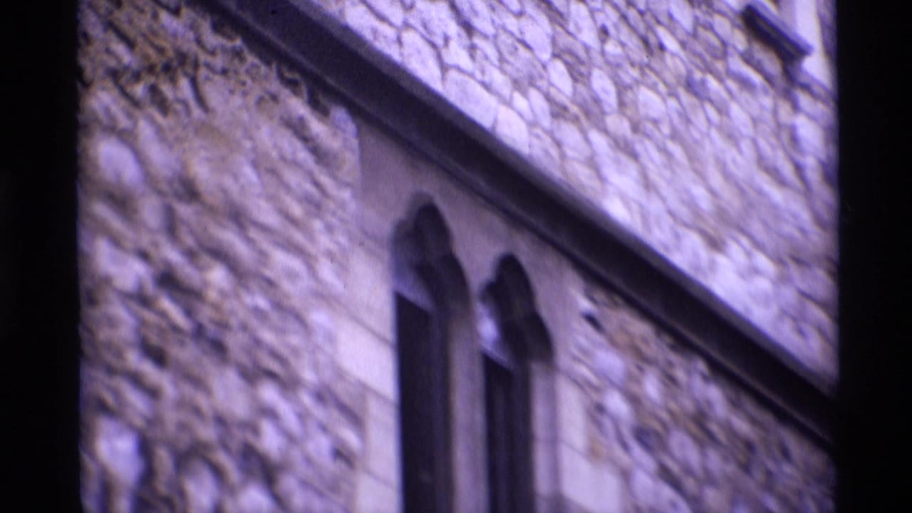 Stone building wall with narrow arched windows and dark film border.