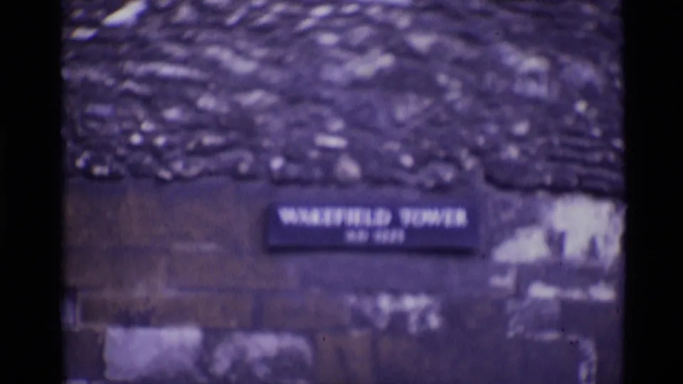 Soft 8mm frame showing a Wakefield Tower sign and stone structure within the Tower of London complex.