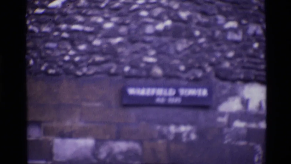 1969 London home-movie frame showing a blurred Wakefield Tower plaque set into rough stonework.