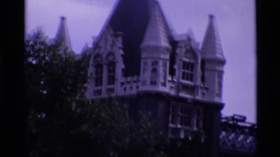 1969 London 8mm frame of Wakefield Tower architecture with pointed turrets, stone windows, trees, and an adjoining raised walkway.