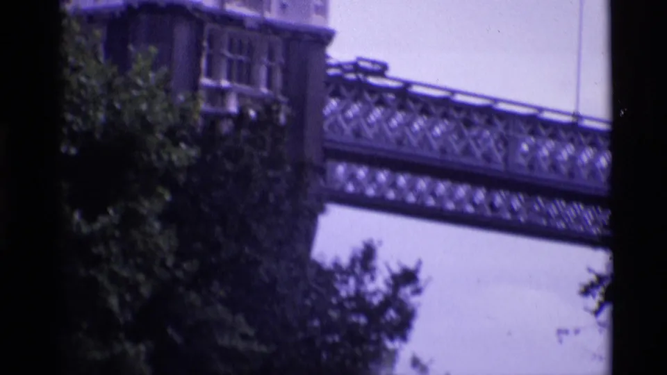 Vintage 8mm London view of a tower edge, leafy trees, and an elevated lattice bridge or walkway beside Wakefield Tower.