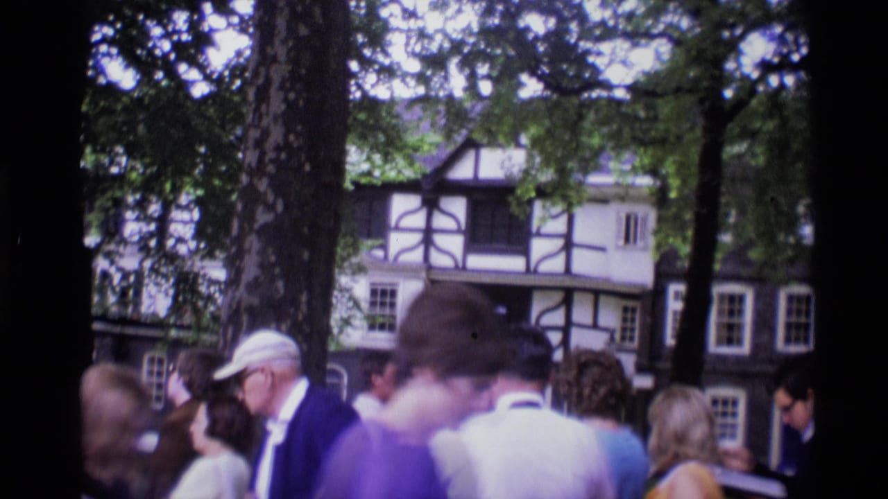Adults stand beneath trees in London, England, with a half-timbered building visible behind them in this 1969 home-movie frame.
