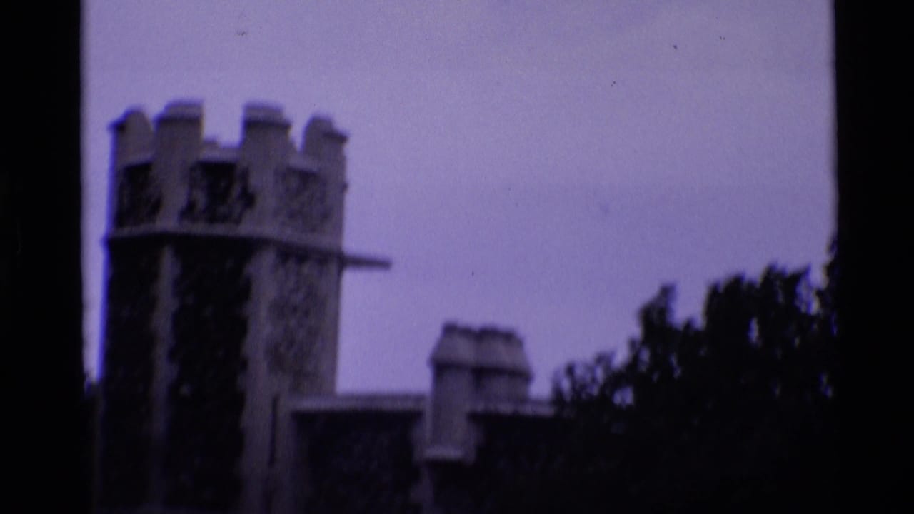 1969 London home-movie frame showing a Tower of London stone tower in soft focus with dark film-edge or foreground obstruction.