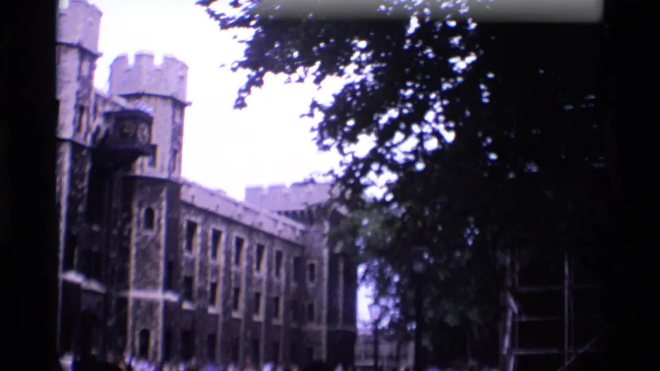 1969 London landmark footage showing the Tower of London facade receding along a walkway beneath dark tree cover.