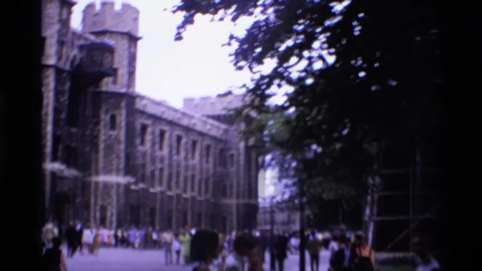 1969 Tower of London courtyard view with groups of tourists walking beside stone walls, towers, and shaded trees.