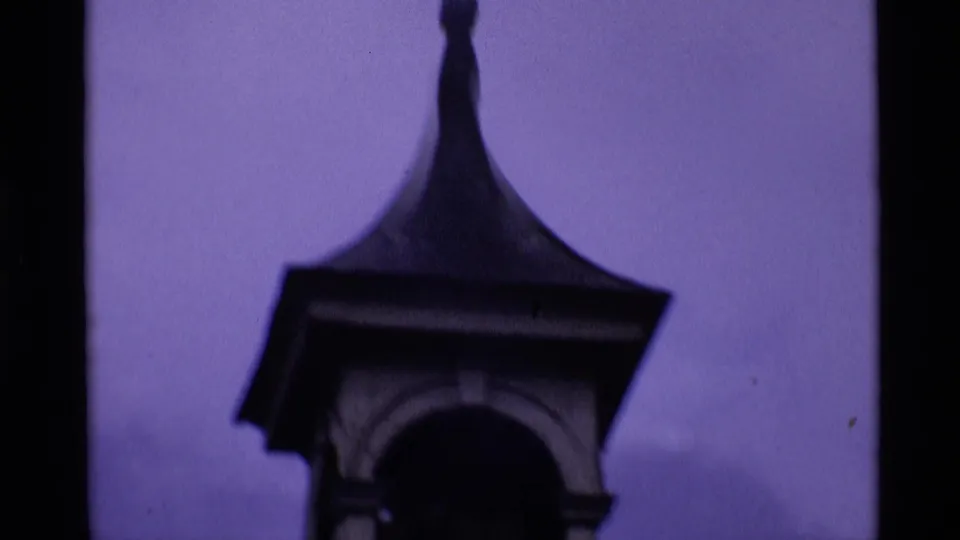 1969 London 8mm frame looking up at a dark spire and arched architectural detail against a purple-tinged sky.
