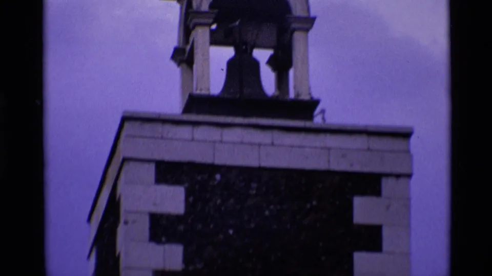1969 London 8mm frame showing the upper portion of a brick tower with a visible bell in the open chamber.