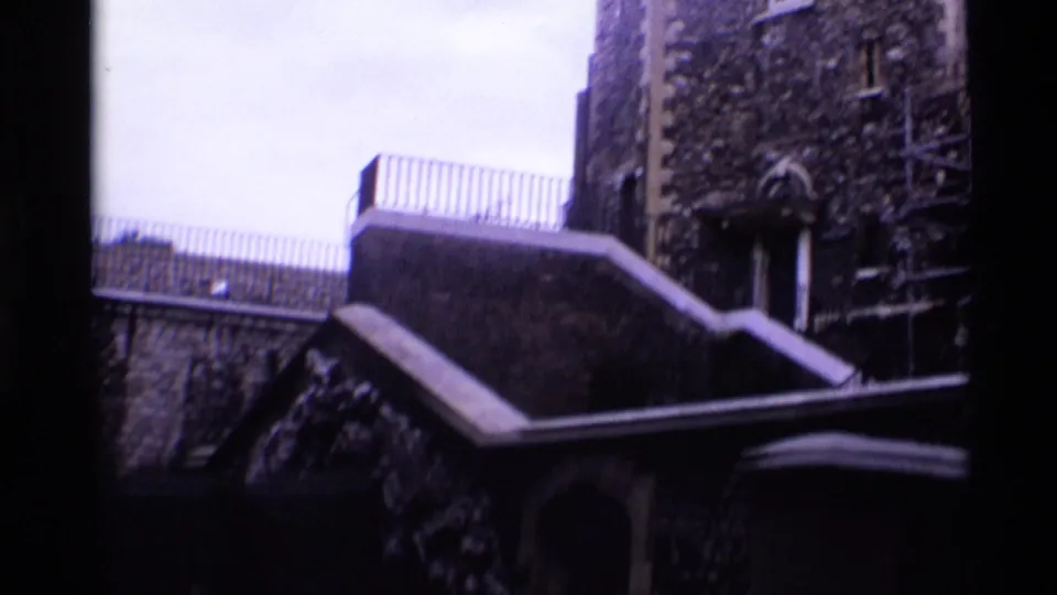 1969 London 8mm frame showing a shadowed stone building exterior with steps, railing, arched doorway, and climbing vegetation.