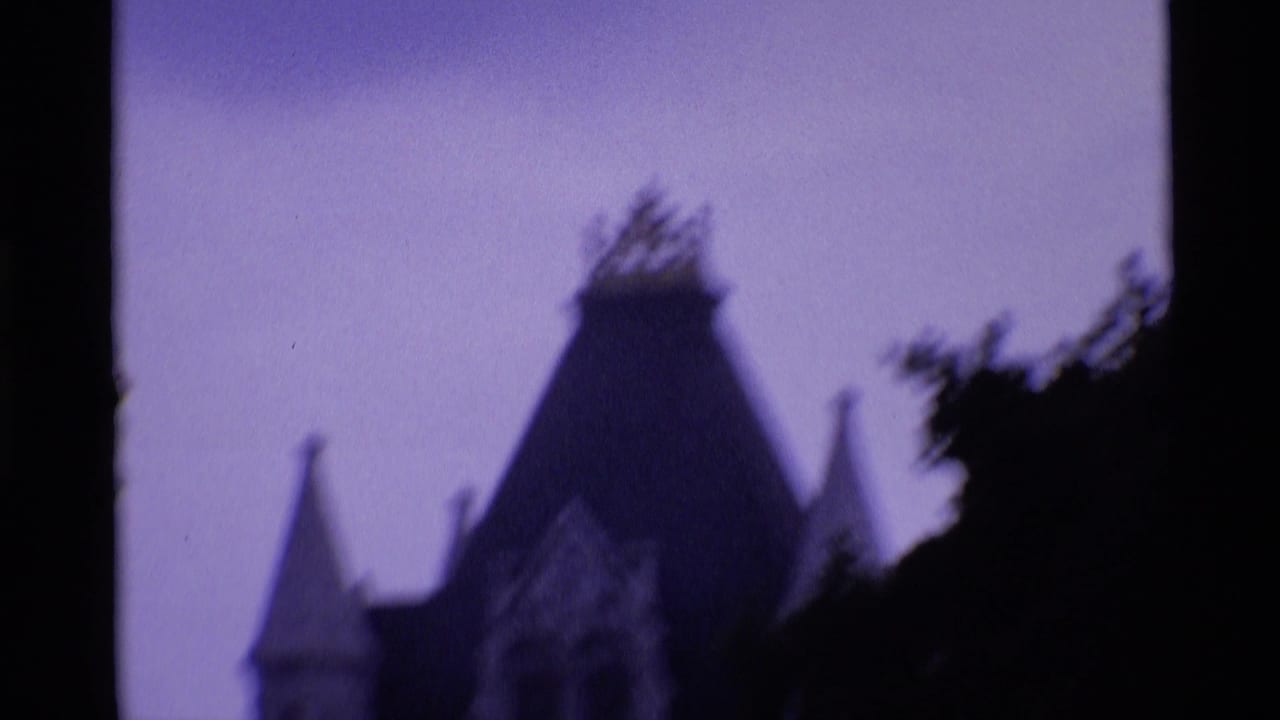 Blurred steep-roofed tower silhouette behind dark trees under a purple sky.
