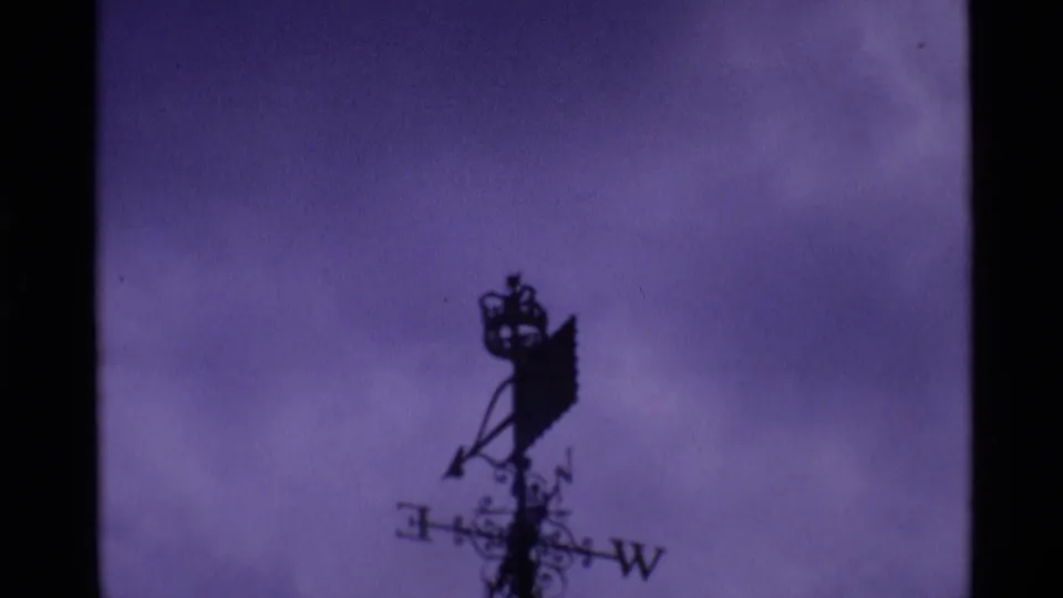 A silhouetted weather vane and roofline appear against a purple sky in 1969 London home-movie footage.
