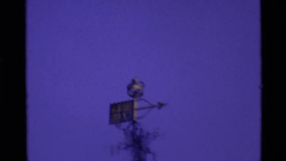 Soft 8mm frame from 1969 London showing a small roof ornament or wind vane against a purple-tinted sky.
