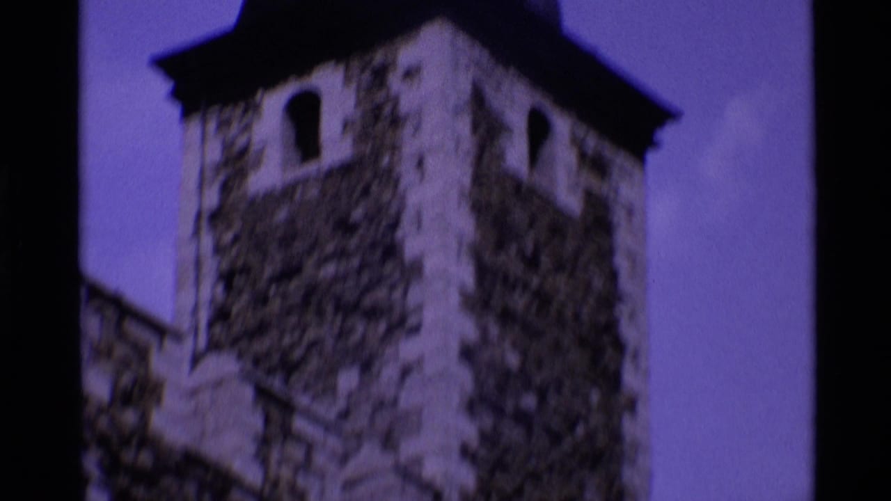 Soft-focus stone tower with arched openings and a dark roofline against sky.