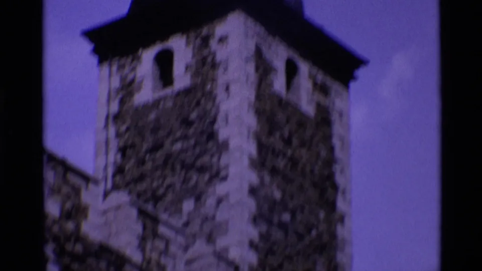 1969 London 8mm frame showing the upper portion of a historic stone tower with arched openings, dark roof edge, and purple-tinted sky.