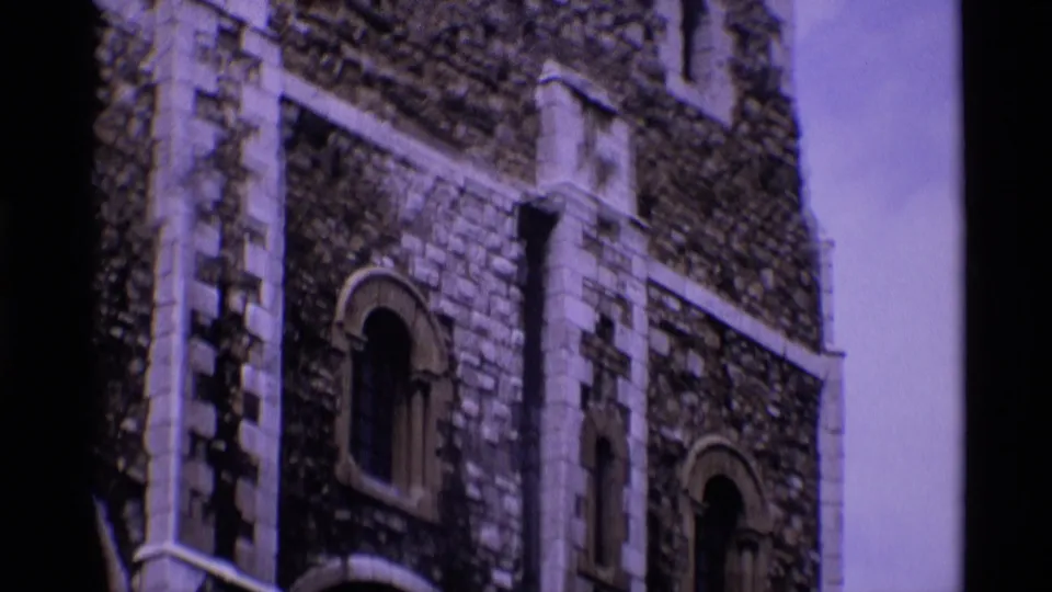 1969 London 8mm frame focusing on a historic stone facade with an arched window, rough masonry, and pale decorative vertical bands.