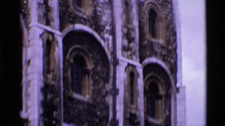 1969 London 8mm frame showing several arched windows on a weathered stone tower facade, with pale trim and a bright sky edge.