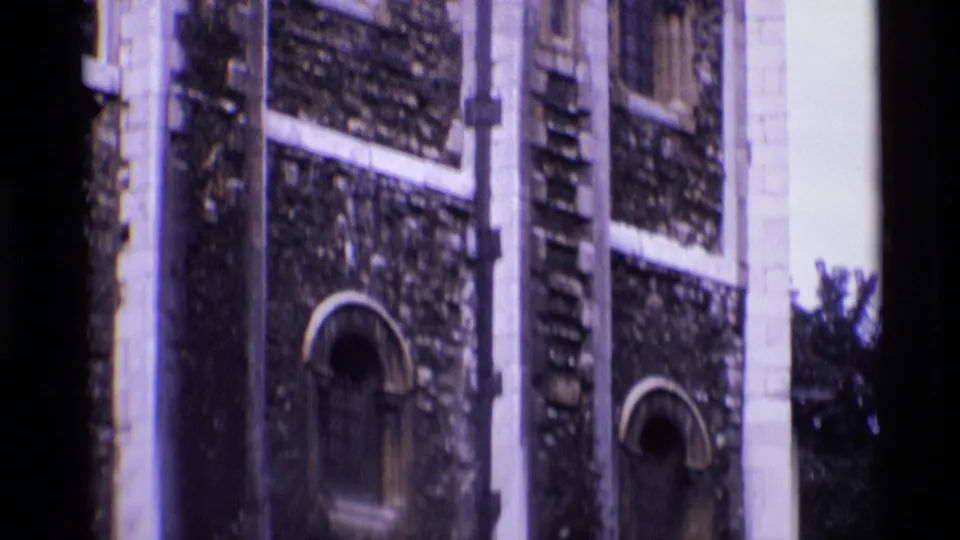 1969 London 8mm frame of the lower portion of a historic stone tower, showing arched windows, pale masonry bands, sky, and dark frame edges.