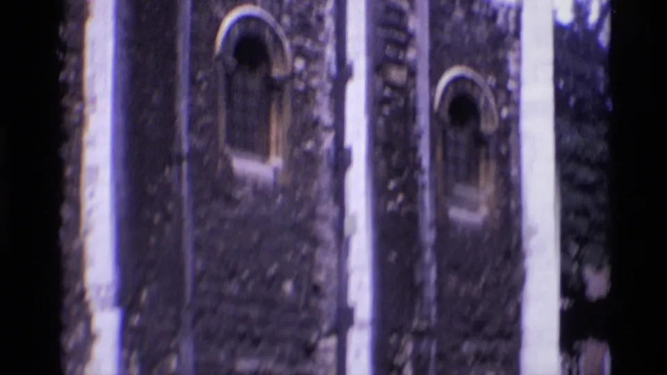 1969 London 8mm frame showing medieval stonework, arched windows, and a shadowed passage at a historic site.