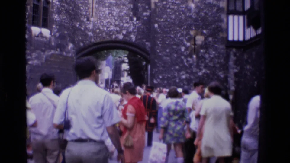 Visitors gather near a stone archway at a London historic landmark, with a Yeoman Warder visible among the crowd.