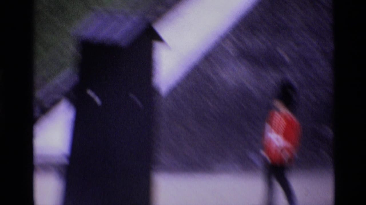 Blurred Royal Guard in red uniform walking near a dark post and stone wall.