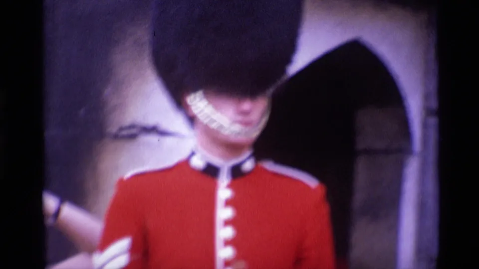Close 1969 London frame showing the ceremonial guard's red tunic, tall black hat, and pale chin strap near stone architecture.