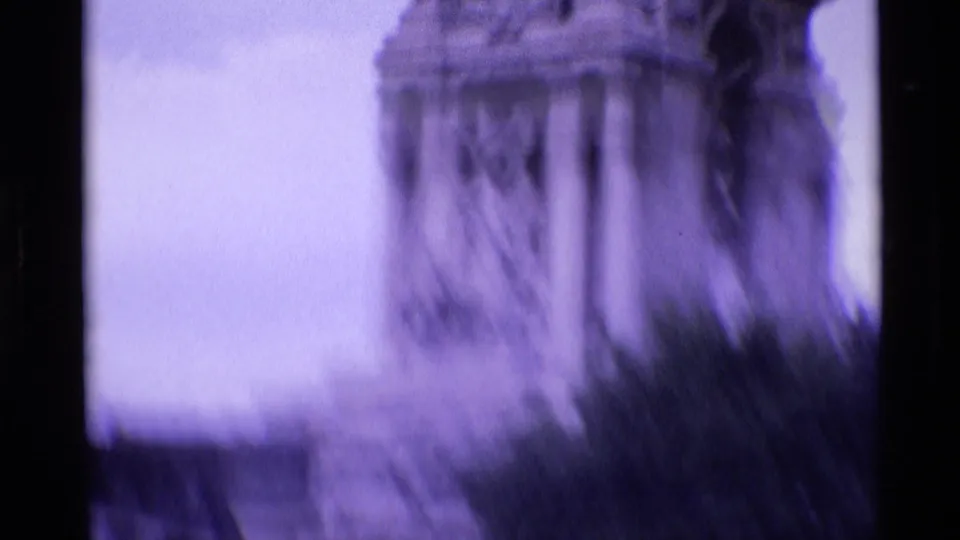 Handheld 1969 London shot looking up at the tower, with stone columns softened by motion blur and foliage below.