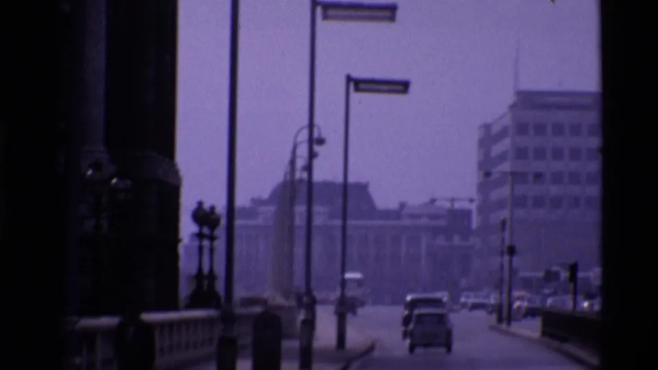 Blurry 1969 London street view near the tower, with cars, lamp posts, a railing, and large buildings in the distance.
