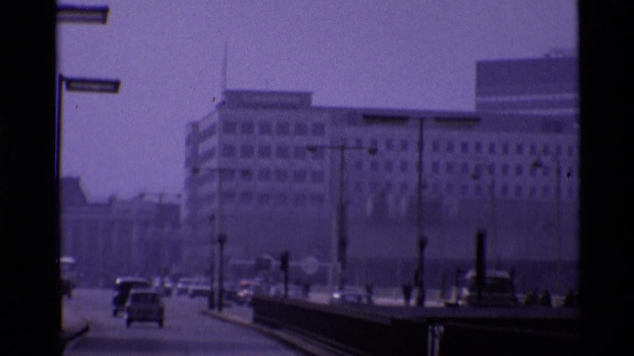 Hazy London street with cars, tall lamps, and large buildings in the distance.
