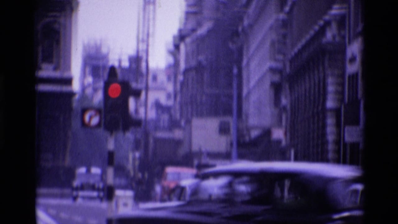 1969 London street view with a red traffic light, classic cars, and masonry buildings in soft 8mm color.