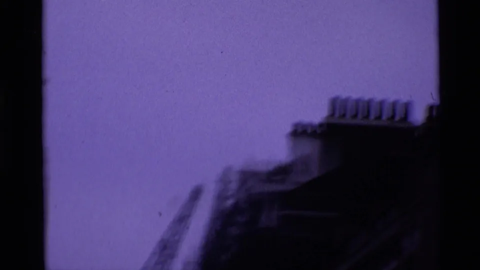 Handheld 8mm view looking upward at a London building roofline and chimneys, blurred by motion.