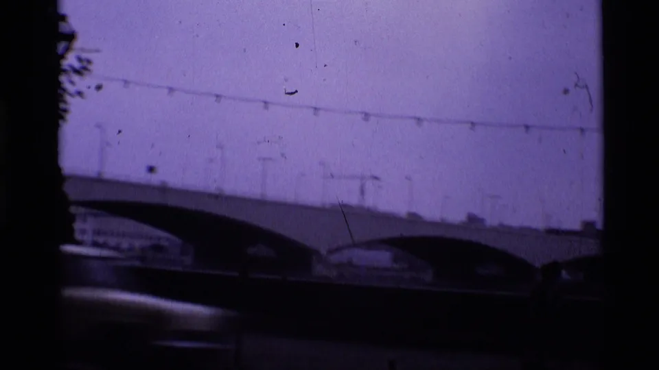 1969 London 8mm view of a river bridge with arched spans, overhead lines, and dark foreground shadow.