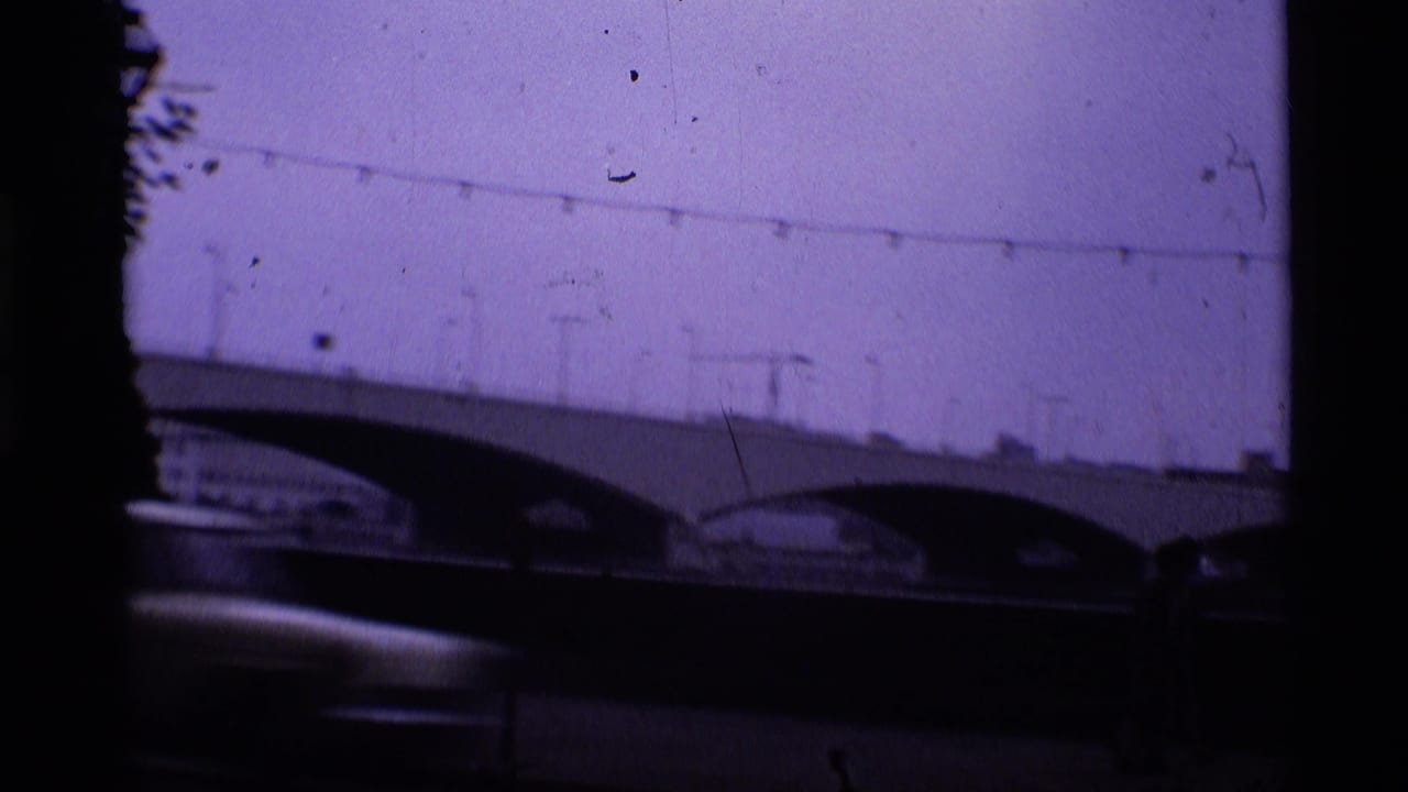 1969 London 8mm frame showing an arched bridge, bridge lamps, and a dark blurred car moving across the foreground.